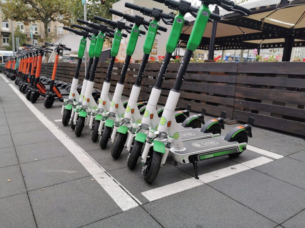Large photo of 20+ green and red scooters parked in front of a restaurant with a brown, slatted, wooden fence, meant to symbolize the need for an accident lawyer and personal injury lawyer.