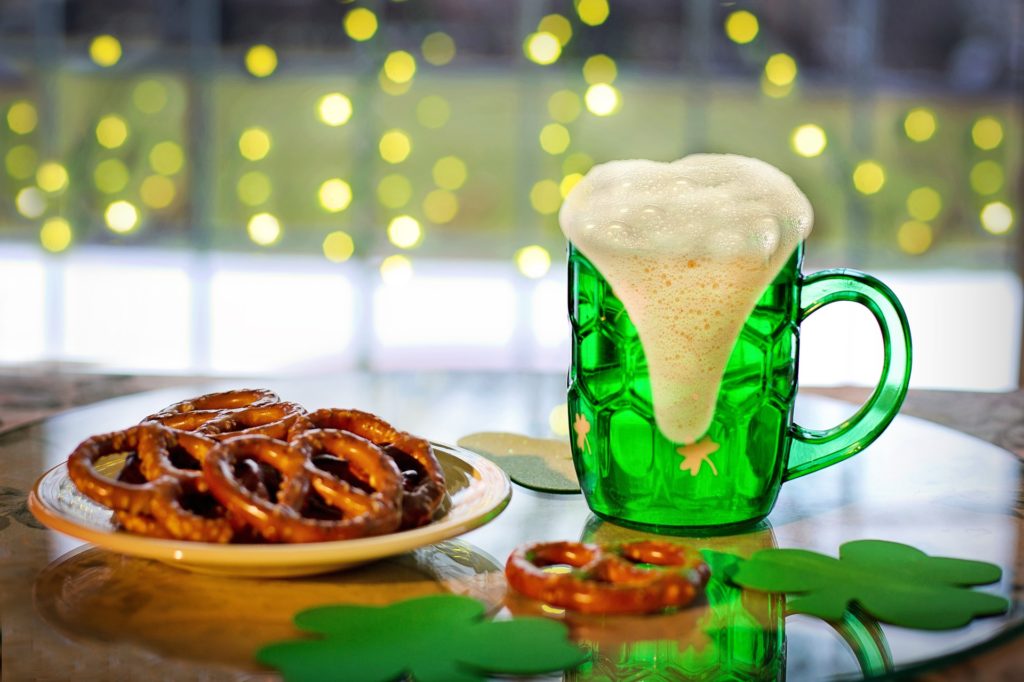 A pint of green beer and pretzels on a table.