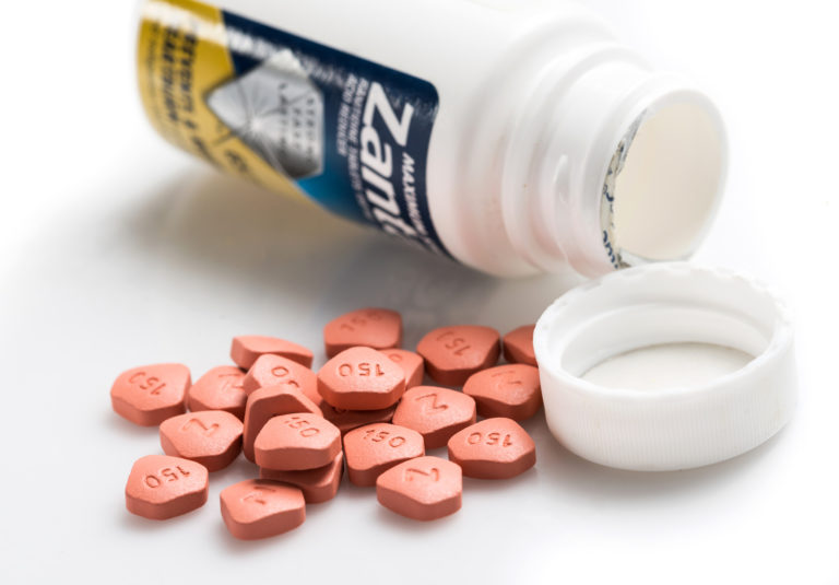 Medium stock photo closeup of an open Zantac bottle on its side, bottle lid, and orange pills, meant to symbolize the need for a defective drug lawyer.