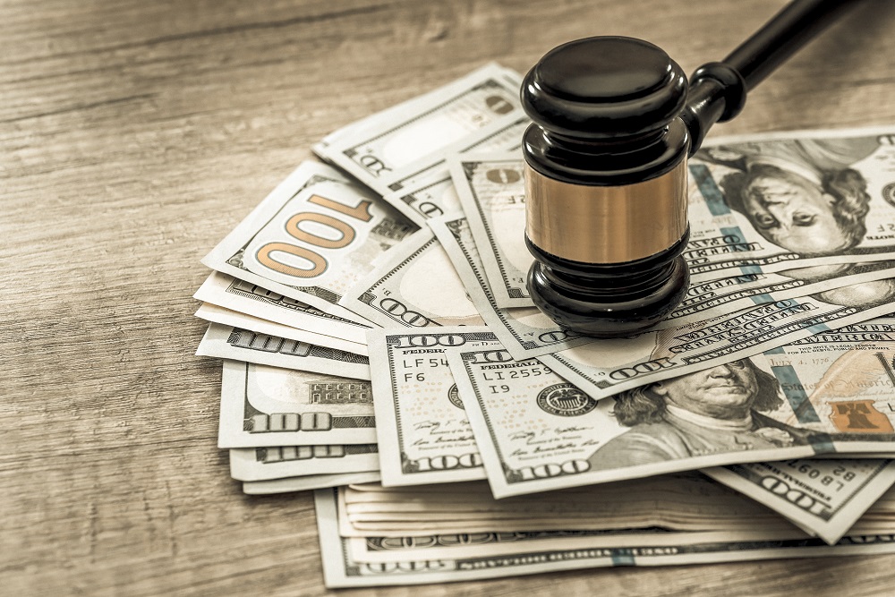 A gavel sits on top of a pile of $100 dollar bills on a wooden table, asking the question, How much to ask for in a personal injury settlement?