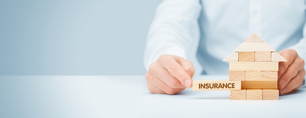 A man from the below the shoulders, wearing a light blue shirt, pulling a wooden slat with the word INSURANCE from a light wood-colored box atop a white table against a light-blue background, posing the question, What is personal injury protection insurance in PA and NJ?
