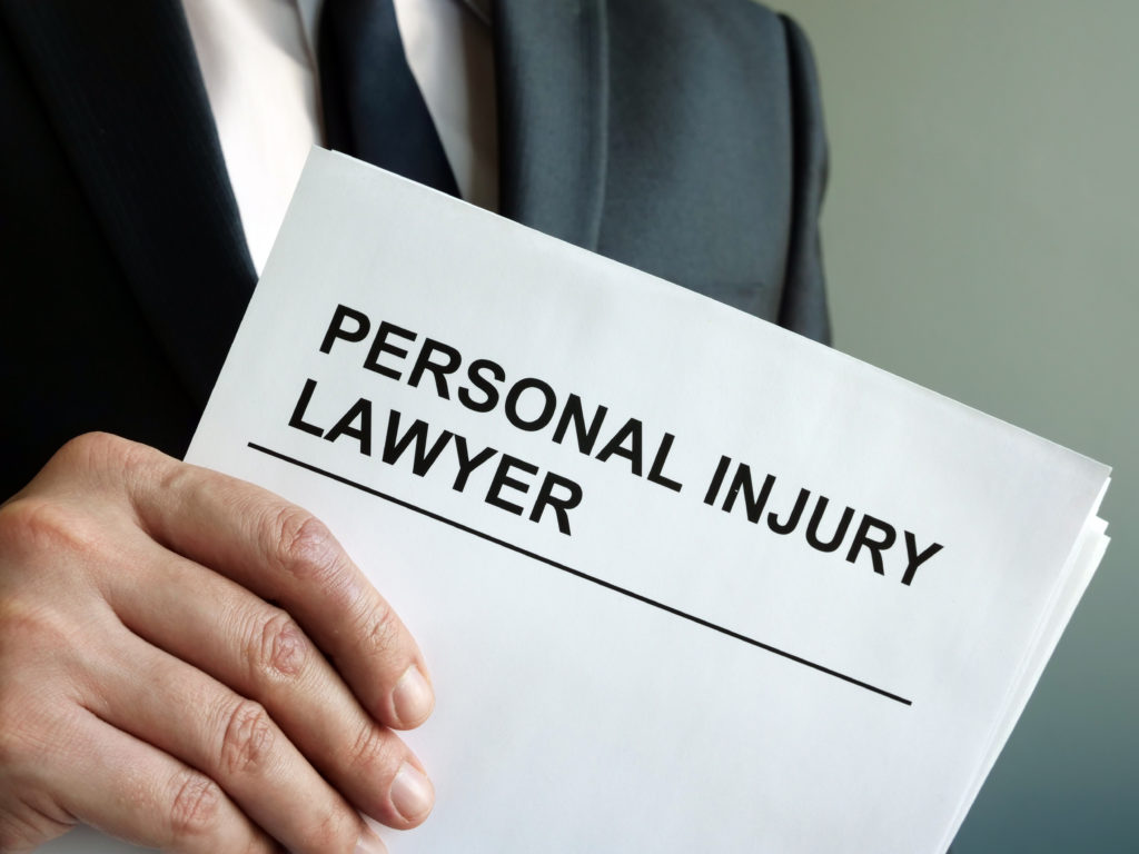 A man from the chest down, wearing a blue suit, white shirt, and blue tie holds a white paper that says PERSONAL INJURY LAWYER in capital letters and black font, posing the question, Do I need a personal injury lawyer in Philadelphia?