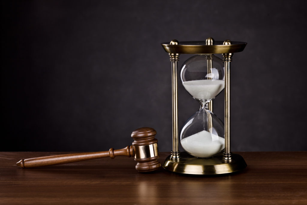 A wooden and brass-plated gavel and a gold, clear glass hourglass with white sand sit on a medium-wood desk, posing the question, How long does a Philadelphia personal injury lawsuit take?