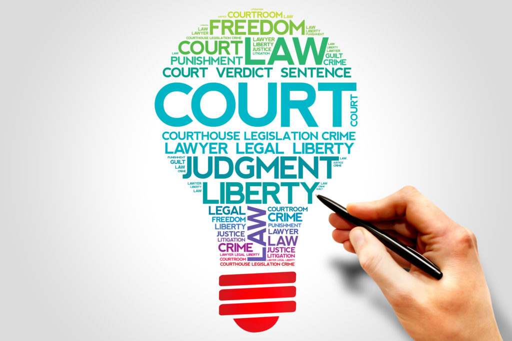 A hand holding a pen next to a colorful set of words like COURT, LAW, JUDGEMENT, LIBERTY and other related terms, arranged in the shape of a lightbulb, posing the question, What is a personal injury lawyer in Philadelphia?