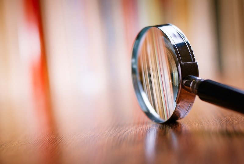 A magnifying glass on the right side of the image, the rim resting on a medium colored wood grain table so that the glass is upright, with the handle pointing to the right, symbolizing things to look for in a Philadelphia personal injury attorney.