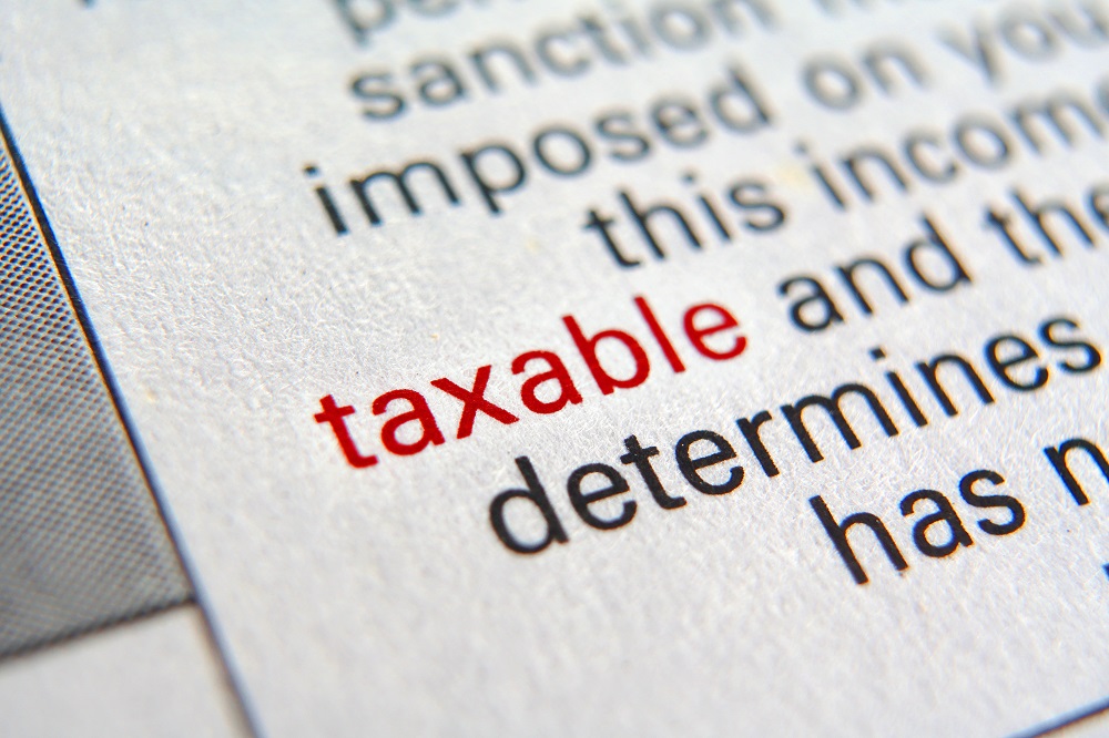 Closeup of a dictionary page angles to the left, focusing on the word TAXABLE in red lettering surrounded by its definition in black lettering, positing the question, Is a personal injury settlement taxable in Philadelphia?