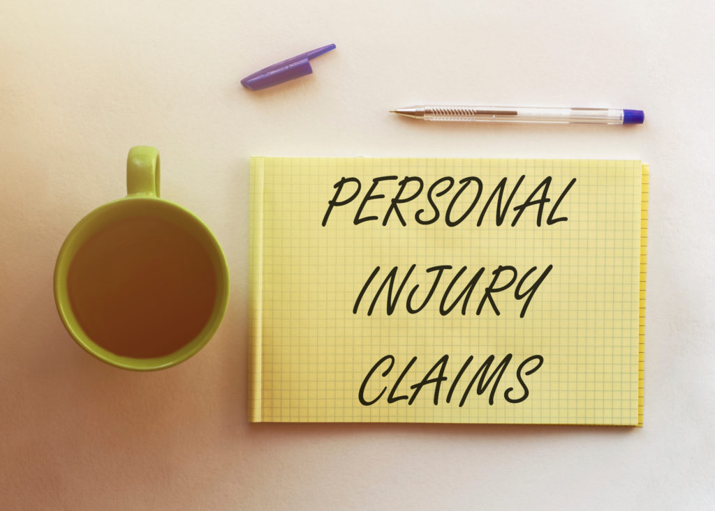 A coffee cup, purple and clear pen, and purple pen cap placed next to a yellow paper tablet that reads PERSONAL INJURY CLAIMS, posing the question, What is a personal injury claim in Philadelphia?