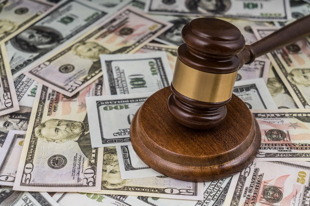 A wooden gavel with a gold accent is hitting a block placed on a table covered in 50 and 100 dollar bills, posing the question, How Much Do Personal Injury Lawyers Charge in Philadelphia?