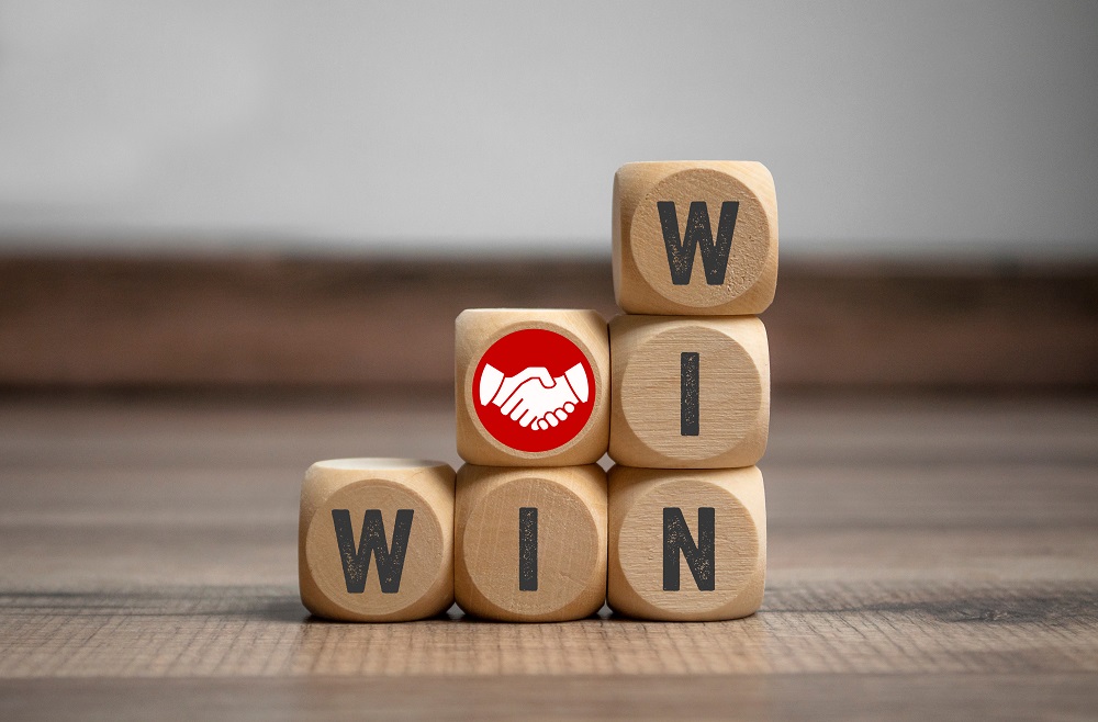 6 small wooden building blocks arranged so that WIN is spelled both vertically and horizontally, with the extra block with a picture of two white hands shaking against a circular red background on top of the 2nd column, symbolizing how to win your personal injury claim in Philadelphia.