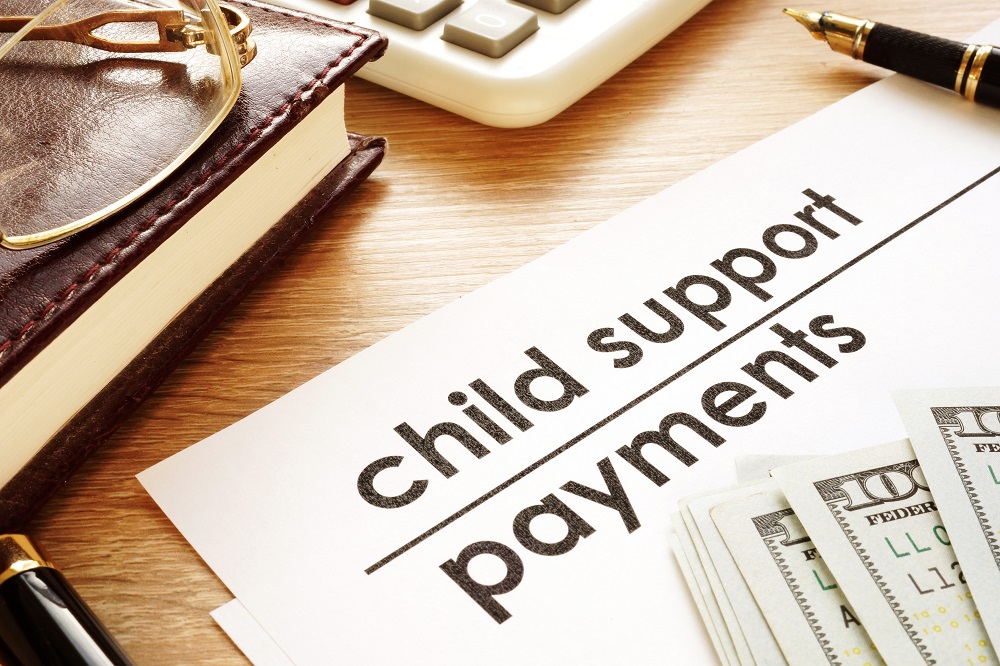 A white paper titled CHILD SUPPORT PAYMENTS with dollar bills placed on a light-grained wood desk, posing the question, Can Child Support Be Taken from a Personal Injury Settlement in Philadelphia?