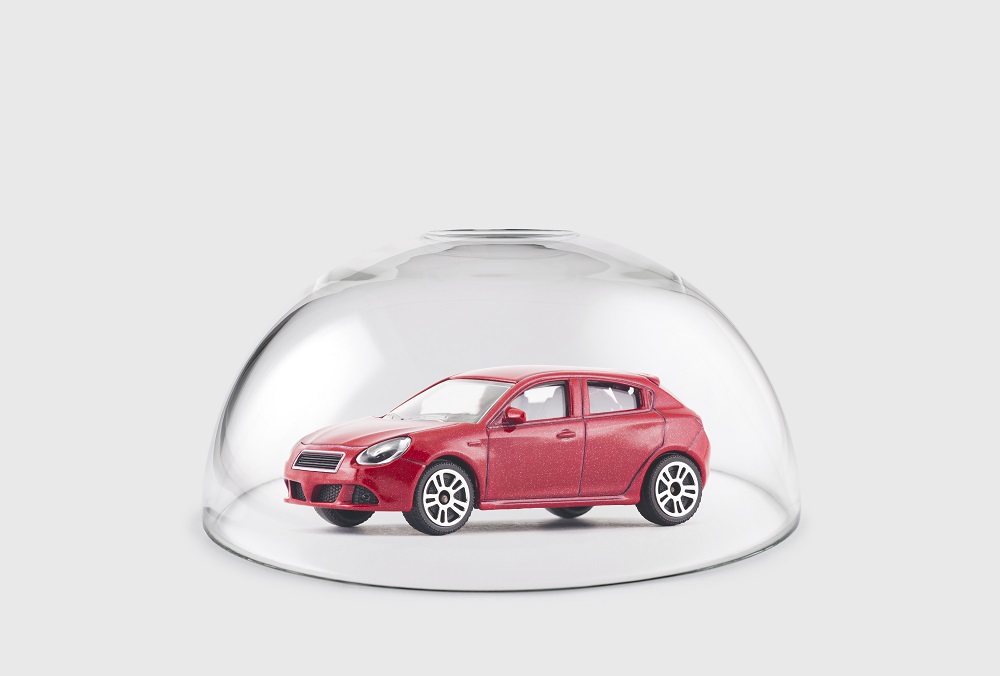 A red hatchback style toy car under a glass dome against a gray background, positing the question, Do I Need Personal Injury Protection Car Insurance in Philadelphia?