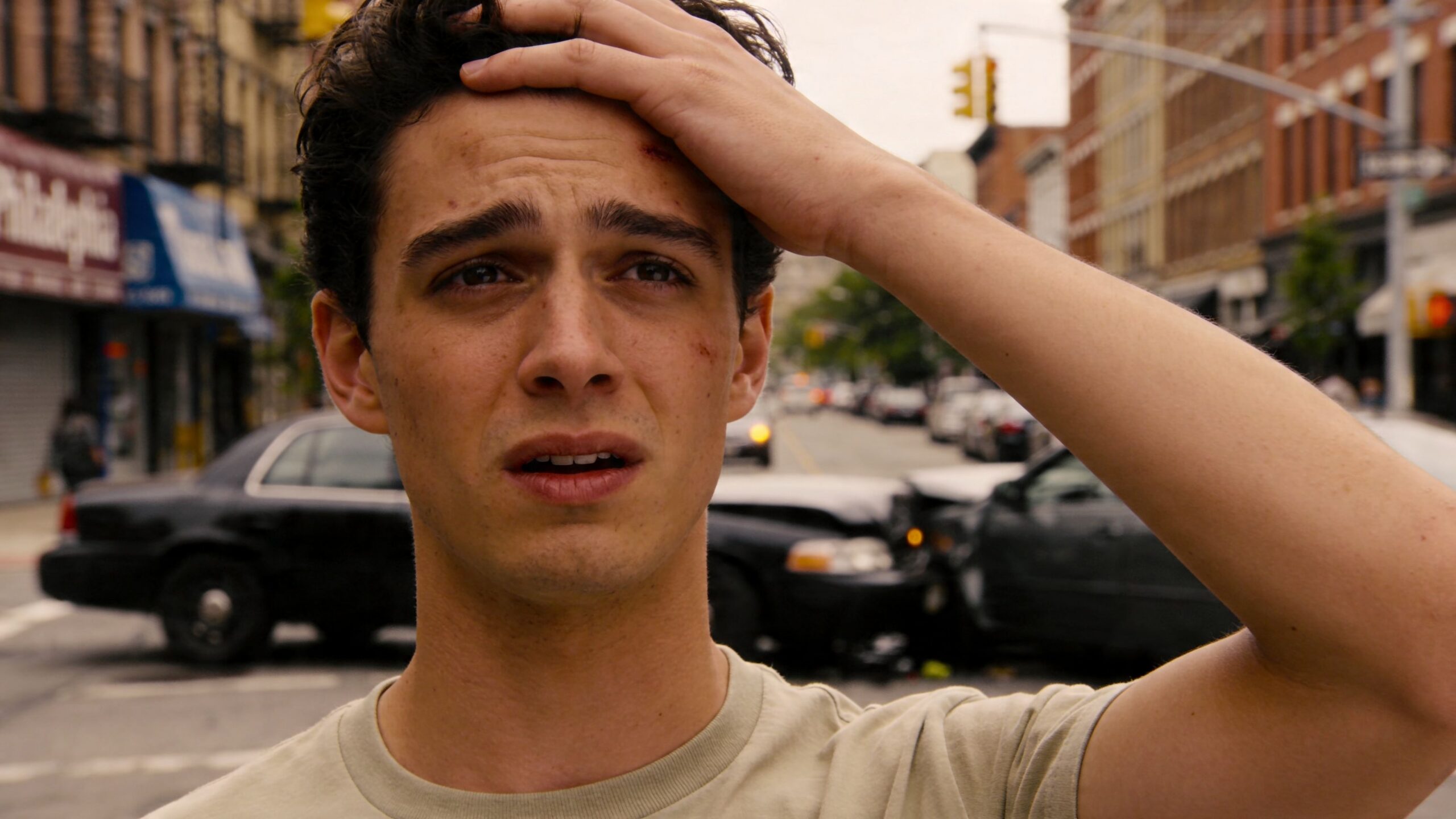A young man looking distressed with a head injury in front of a car accident in Philadelphia.