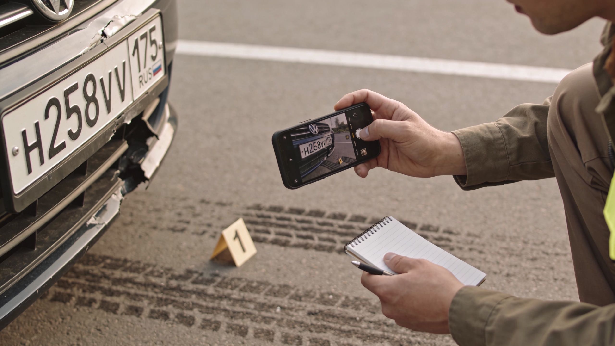 A police officer documenting car accident evidence at the scene by taking a photo of a license plate.